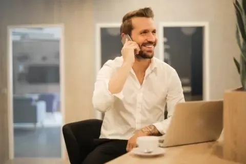 Ein Angestellter telefoniert am Schreibtisch mit einer Tasse Kaffee